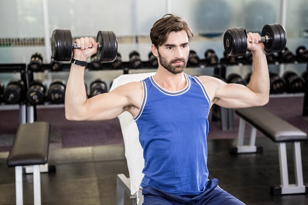 Mięśniowego mężczyzna podnośni dumbbells na ławce przy gym