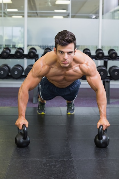 Mięśniowy mężczyzna podnosi z czajników dzwonami w gym robić pcha