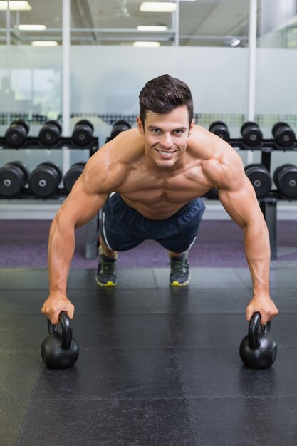 Mięśniowy mężczyzna podnosi z czajników dzwonami w gym robić pcha