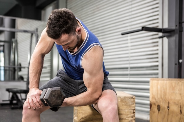 Mięśniowy mężczyzna podnośny dumbbell na drewnianym bloku przy crossfit gym