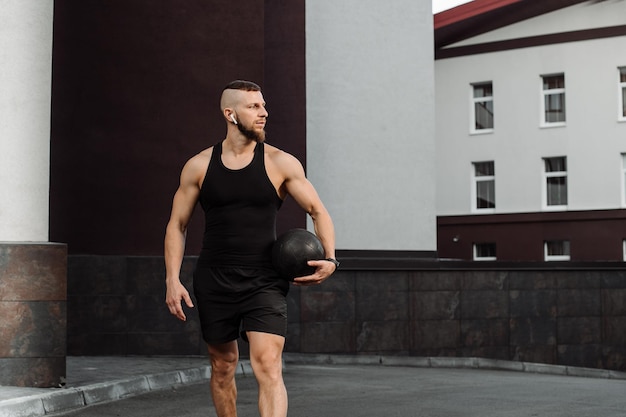 Mięśniowy trener fitness chodzi na świeżym powietrzu z ciężką piłką fitball