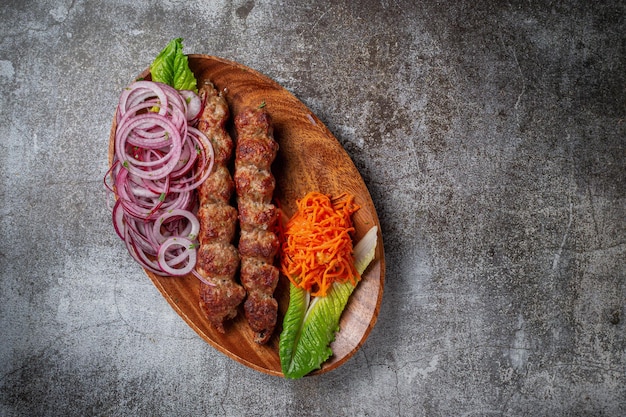 Mięsny Kebab I Grill Z Cebulą, Koreańską Marchewką I Zieloną Sałatą W Talerzu Na Tle Szarego Kamiennego Stołu