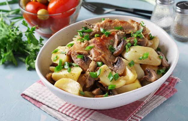 Mięso królika z ziemniakami i pieczarkami w lekkim talerzu na jasnoniebieskim tle. Zbliżenie