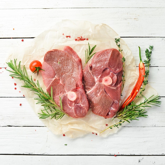 Mięso Surowy stek jagnięcy bez kości z rozmarynem i przyprawami Na białym drewnianym tle Widok z góry