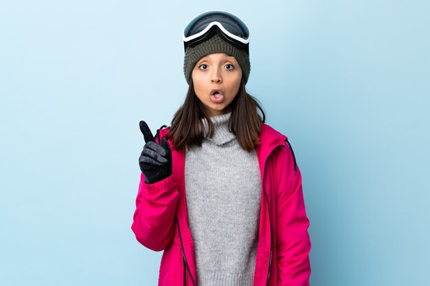 Mieszana biegowa narciarki dziewczyna z snowboardowymi szkłami nad odosobnioną błękit ścianą myśleć pomysł wskazuje palec up