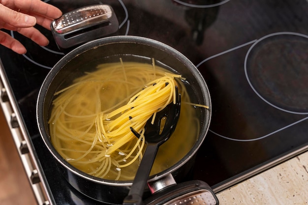 Mieszanie spaghetti gotowanego w rondlu łyżką cedzakową