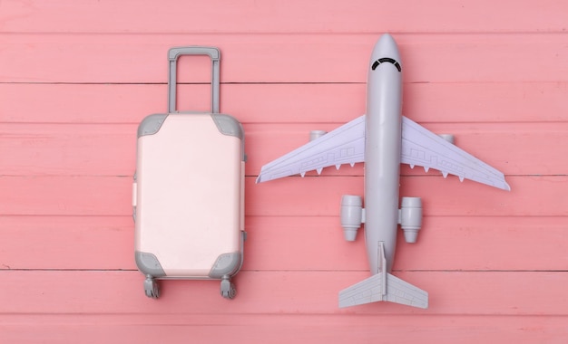 Mieszkanie świeckich wakacje wakacje i koncepcja planowania podróży. Mini plastikowa walizka podróżna i samolot na różowym tle drewnianych. Widok z góry