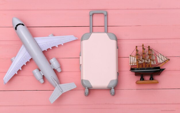Mieszkanie świeckich wakacje wakacje i koncepcja planowania podróży. Mini plastikowa walizka podróżna i samolot, statek na różowym tle drewnianych. Widok z góry