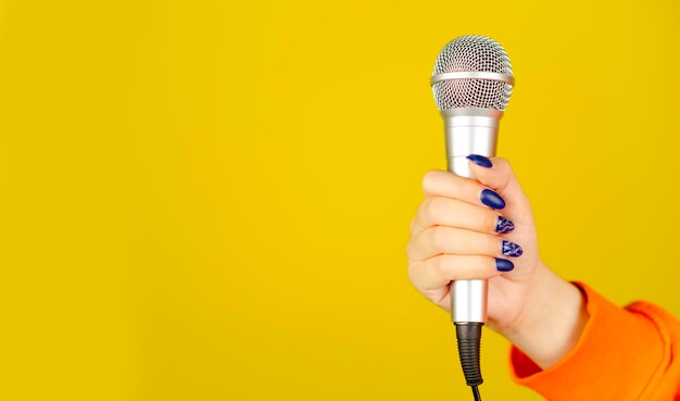 Mikrofon w kobiecej dłoni na żółtym tle z miejscem na tekst Nie do poznania kobieta trzyma mikrofon do śpiewania