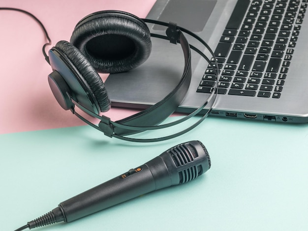 Zdjęcie mikrofon w słuchawkach i otwarty laptop na niebieskim i różowym tle
