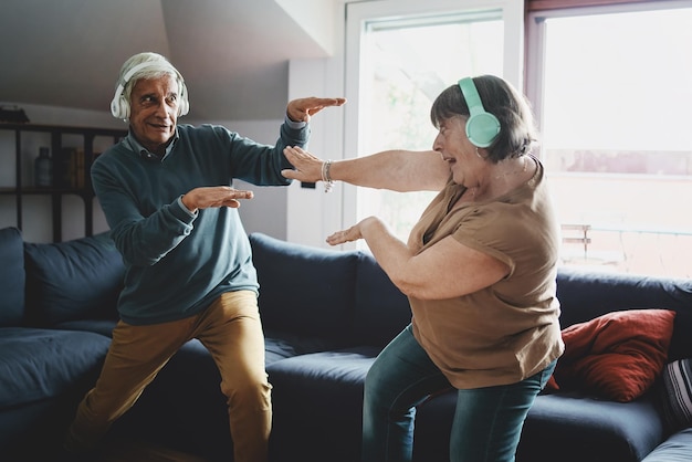 Miła, aktywna para starszych, ciesząca się fantazyjnym tańcem w salonie, nosząca słuchawki bezprzewodowe, koncepcja życia domowego dziadków