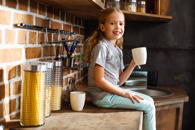 Miła Mała Dziewczynka Uśmiecha Się Podczas Picia Herbaty W Kuchni