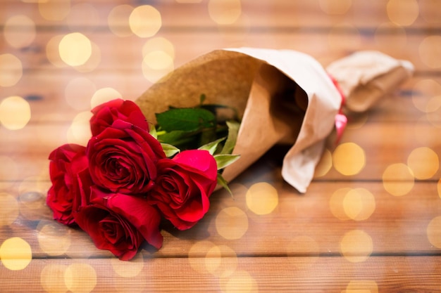 miłość, data, kwiaty, walentynki i święta koncepcja - zbliżenie bukietu czerwonych róż owiniętych w brązowy papier na drewnianym stole