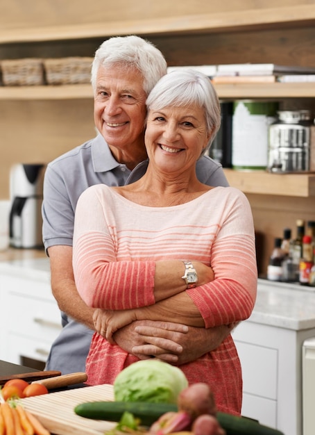 Miłość do gotowania i portret starszej pary w kuchni dla zdrowia lub odżywiania sałatek Szczęśliwy uśmiech i przejście na emeryturę ze starszym mężczyzną przytulającym kobietę i krojącym warzywa w domu na obiad lub przepis