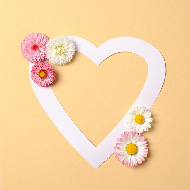 Miłość koncepcja natury. Kwiaty stokrotki i biała kartka papieru w kształcie serca na pastelowym żółtym tle.