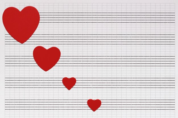 Miłość, muzyka i serca. Serca czerwonego papieru leżą na czystym notatniku muzycznym.