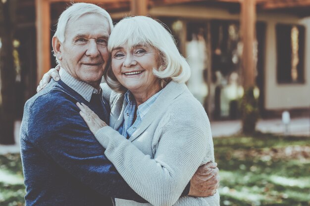 Miłość na zawsze. Szczęśliwa para seniorów, która łączy się ze sobą i uśmiecha, stojąc na zewnątrz i przed swoim domem