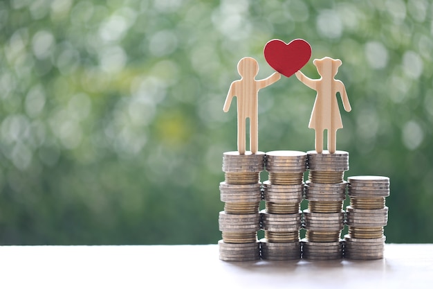 Zdjęcie miłość para trzymając kształt serca stojąc na stosie pieniędzy monet na naturalnym zielonym tle