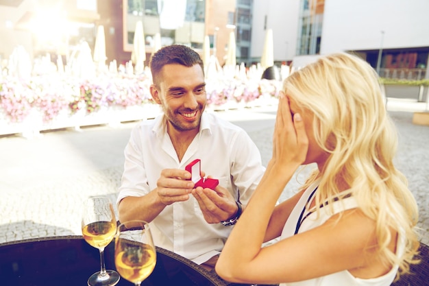 miłość, rocznica, niespodzianka, koncepcja ludzi i wakacji - szczęśliwy mężczyzna z pierścionkiem zaręczynowym składający propozycję kobiecie w restauracji