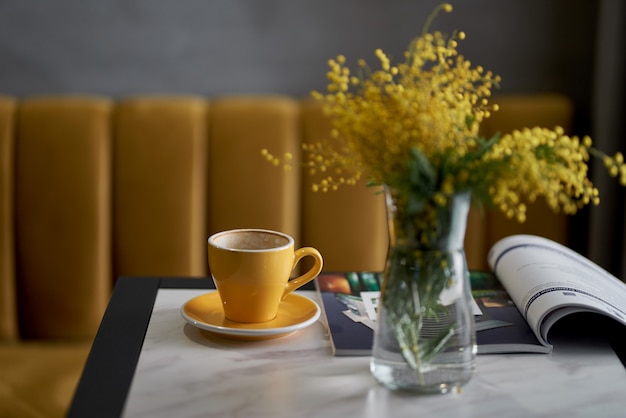 mimoza w wazonie i kawa w żółtej filiżance na stole w kawiarni lub restauracji