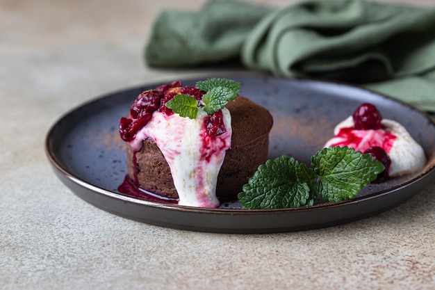 Mini ciasto czekoladowe lub brownie ze śmietaną, wiśnią i miętą na talerzu ceramicznym. Fondant czekoladowy.