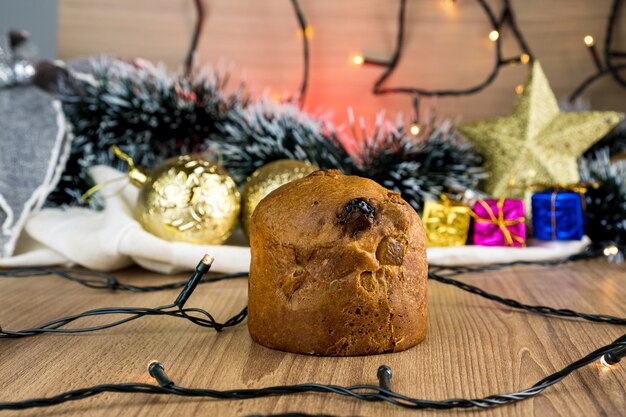 Zdjęcie mini panettone na drewnianym stole z ozdób choinkowych. kule czerwone, srebrne i złote, pudełka na prezenty, lampki, choinki i inne. selektywne skupienie.