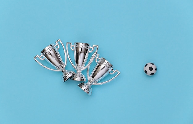 Zdjęcie mini piłka i puchary mistrzostw na niebieskim tle. koncepcja sportu minimalizm. widok z góry. płaskie ułożenie