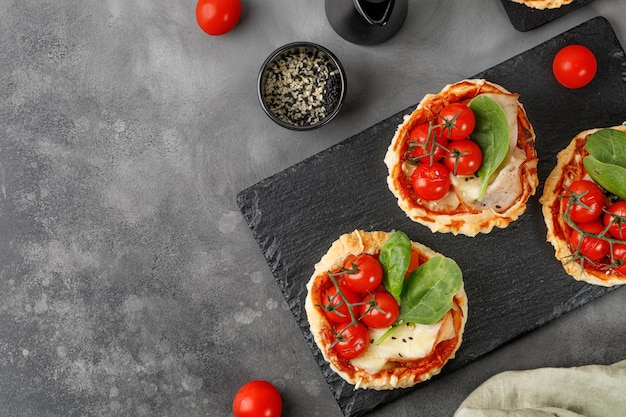 Mini Pizzas mała domowa pizza z otwartym ciastem z pomidorami i serem na łupkowej desce i ciemnym tle