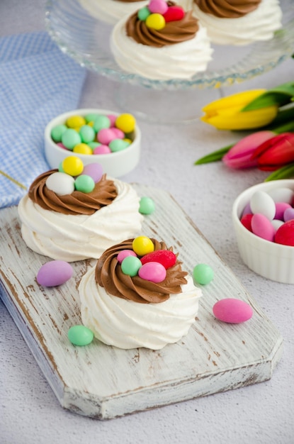 Mini Ptasie Gniazdo Pavlova z kremem czekoladowym i kolorowym cukierkiem na jasnym tle Wielkanocny tort