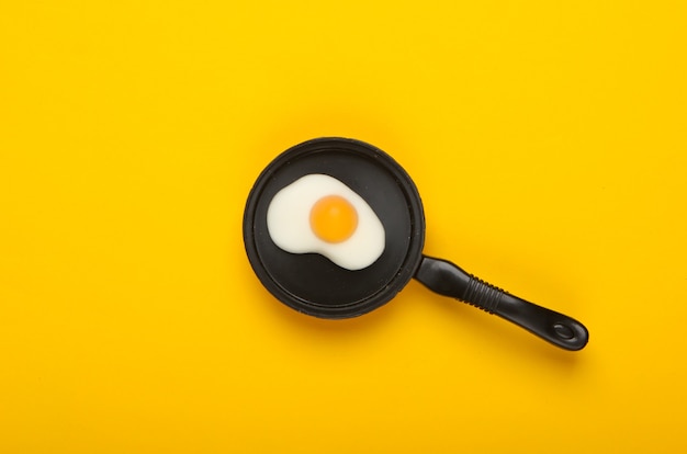 Miniaturowa zabawkowa patelnia z jajkiem sadzonym na żółtym tle. Widok z góry. Koncepcja żywności minimalizmu, śniadanie. Strzał studio