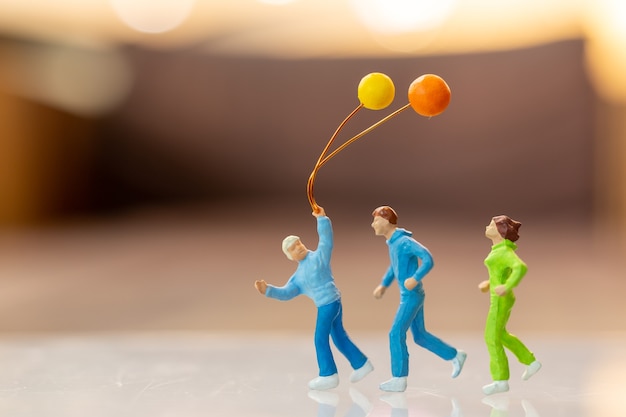 Miniaturowe ludzie szczęśliwa rodzina bieganie i granie z balonem, dzieciństwo i koncepcja rodziny.