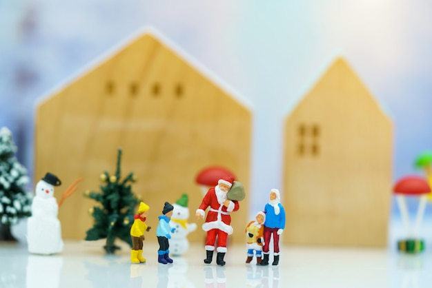 Miniaturowe osoby: Święty Mikołaj z dziećmi bawiący się śniegiem i choinką.