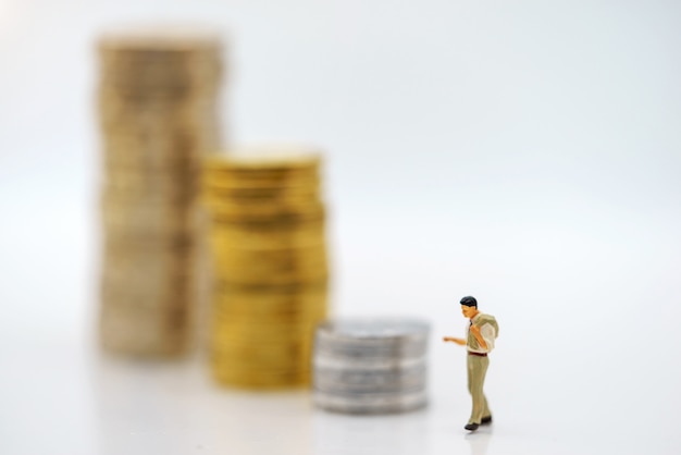 Miniaturowi ludzie: Biznesmeni stoi z stertą monet, pojęciem Finanse i inwestyci.