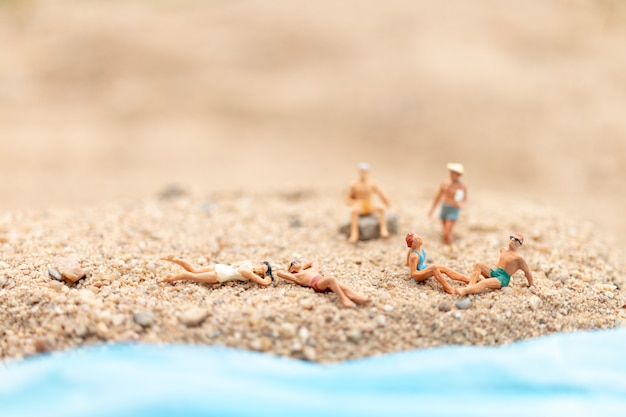 Miniaturowi ludzie jest ubranym strój kąpielowego relaksuje na plaży