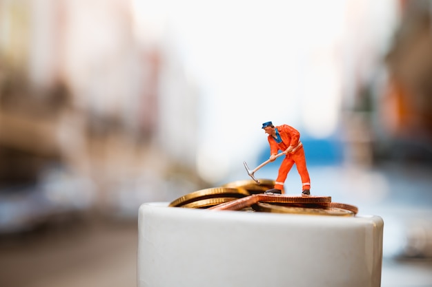 Zdjęcie miniaturowi ludzie, mężczyzna pracuje na sterta monetach