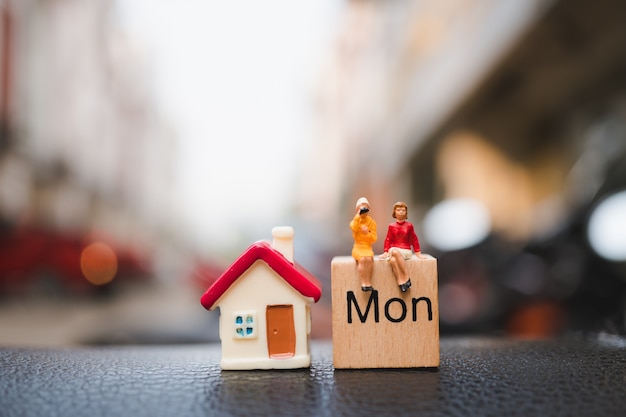 Miniaturowi ludzie, pary kobiety obsiadanie na drewnianym bloku kalendarzu z mini domem używać jako biznes an