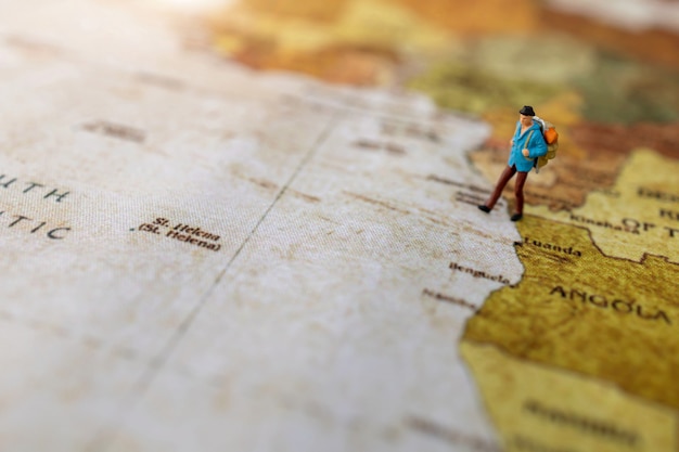 Miniaturowi ludzie: podróżujący z plecakiem stojącym na mapie świata w stylu vintage, podróż i koncepcja lato.