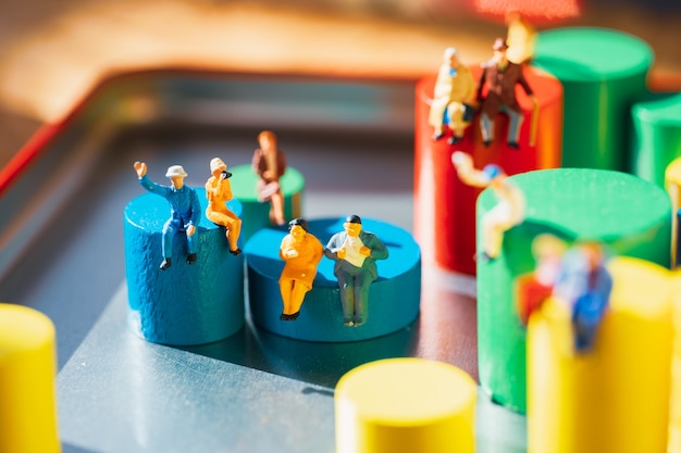 Miniaturowi ludzie siedzący na kolorowym drewnianym bloku jako koncepcja rodzinna i społeczna