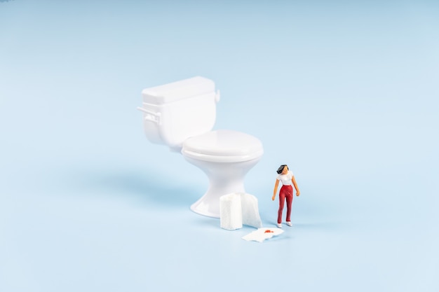 Miniaturowy model kobiety przy toalecie z papierem toaletowym z koncepcją krwi hemoroidów