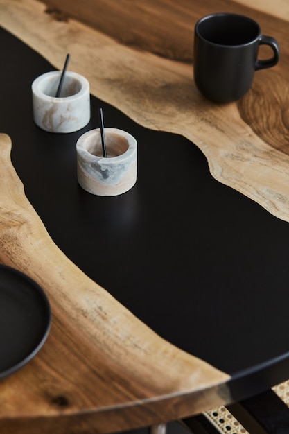 Minimalistyczna kompozycja na designerskim stole z drewna i żywicy epoksydowej z czarnymi filiżankami i łyżką, marmurowe naczynie. Nowoczesne wnętrze jadalni. Detale..