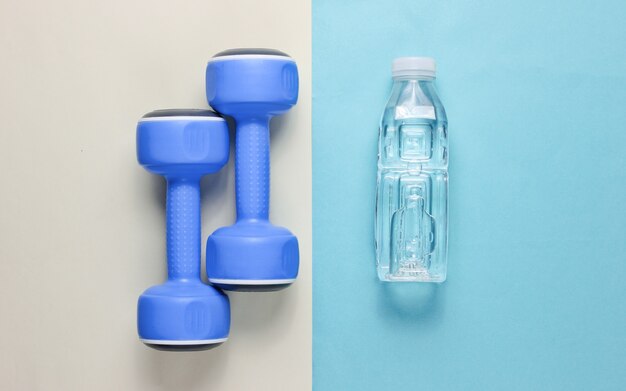 Minimalistyczna koncepcja fitness. Hantle, butelka wody na kolorowym