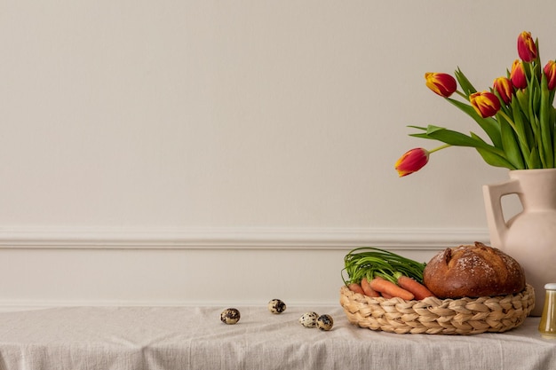 Minimalistyczna wiosenna kompozycja wielkanocnego wnętrza salonu z przestrzenią do kopiowania beżowy wazon z tulipanami pleciony kosz z chlebem marchewkowym, jajkami przepiórczymi i akcesoriami osobistymi Wystrój domu Szablon