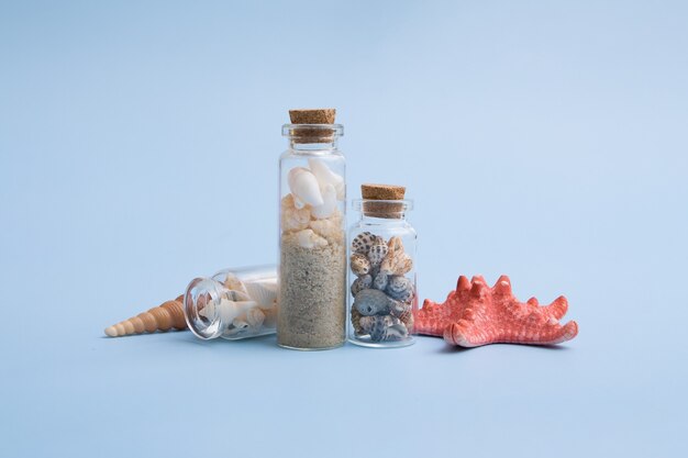 Minimalistyczne letnie tło z mini butelkami, małymi, muszlami, piaskiem, gwiazdą morza