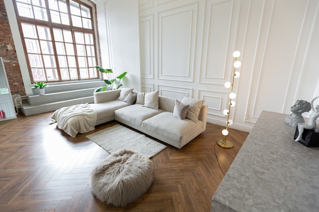 Minimalistyczne wnętrze ultranowoczesnego mieszkania na planie otwartym z biało-szarymi ścianami z płaskorzeźbą i szarymi stylowymi meblami tapicerowanymi i ogromnymi oknami