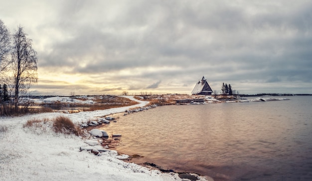 Minimalistyczny śnieżny zimowy krajobraz z autentycznym domem na brzegu w rosyjskiej wsi Rabocheostrovsk.