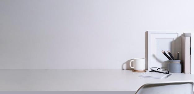 Minimalne miejsce pracy z ramką na zdjęcia roślina doniczkowa filiżanka kawy i materiały eksploatacyjne na białym stole Skopiuj miejsce na tekst reklamowy