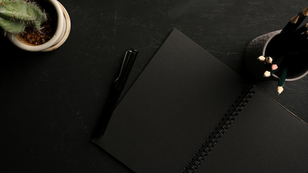 Minimalny ciemny obszar roboczy z czarnymi pustymi stronami w notatniku z papeterią na stole. widok z góry