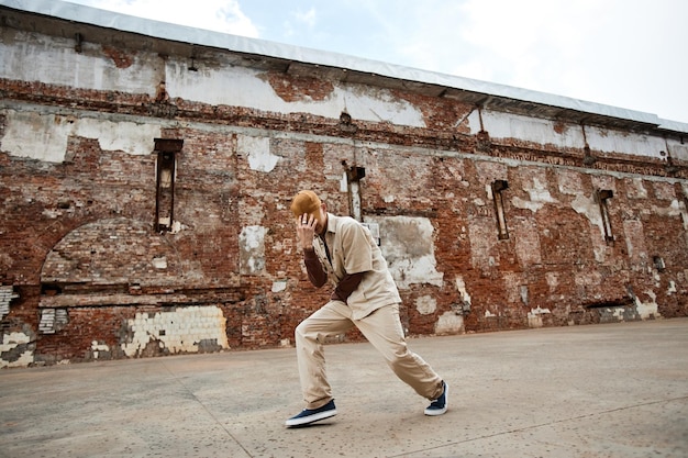 Minimalny szeroki kąt ujęcia młodego mężczyzny tańczącego hiphop na zewnątrz w odrapanym otoczeniu miejskim i ukrywającego twarz