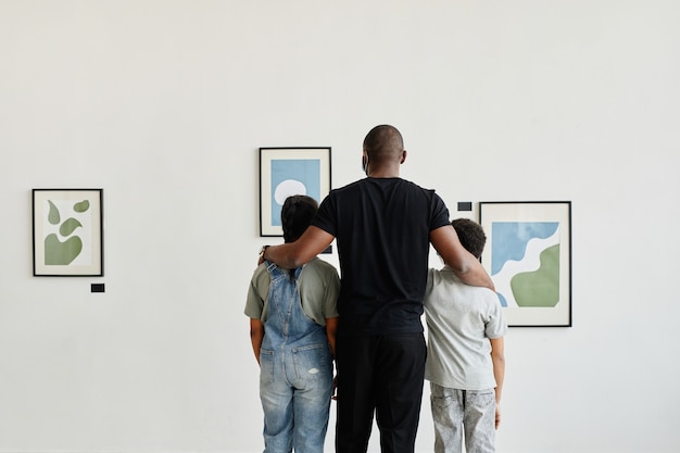 Minimalny widok z tyłu na afroamerykańską rodzinę oglądającą obrazy w galerii sztuki nowoczesnej, kopia przestrzeń