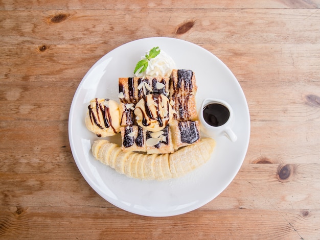 Zdjęcie miodowa grzanka dekorował z bananem i czekoladą w białym naczyniu na drewnianym stole